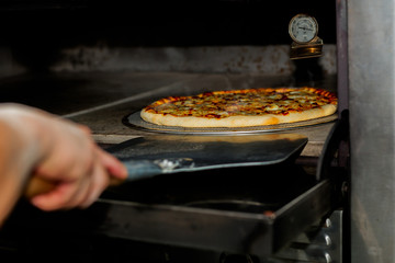 Chef taking pizza out of the oven with pizza shovel equipment.