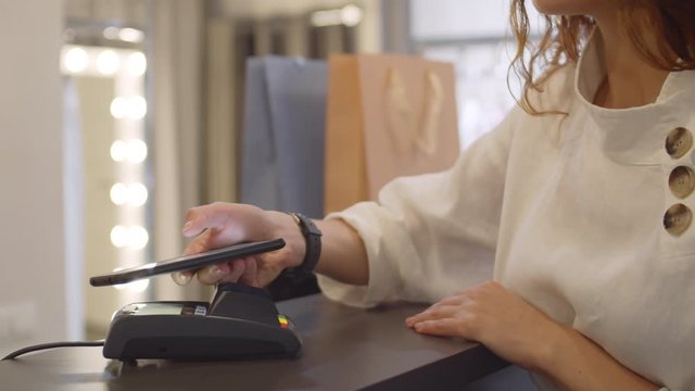 Close up of woman paying in shop using mobile phone