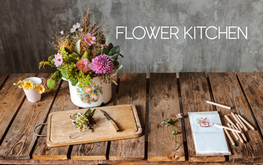 An ancient pot with a composition of flowers on a wooden rustic table against a concrete wall.