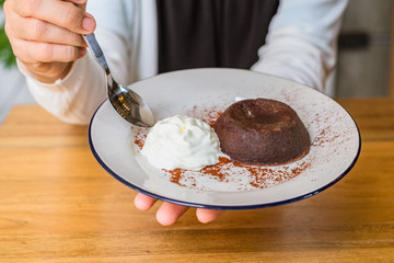 Closeup of woman hand using small spoon scooping chocolate Lava cake and ice-cream on white plate