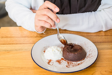 Closeup of woman hand using small spoon scooping chocolate Lava cake and ice-cream on white plate