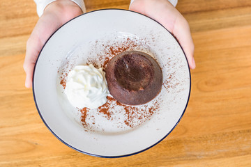 Chocolate Lava cake and ice-cream on white plate held by woman hand