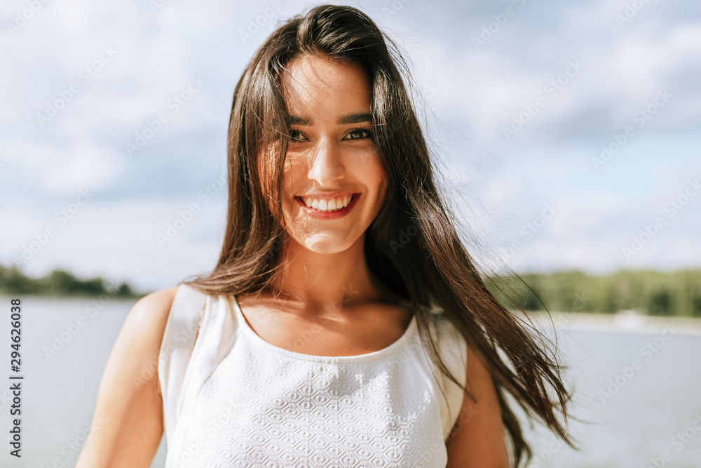 Wall mural happy beautiful young woman smiling broadly with healthy toothy smile and with a windy blowing long 