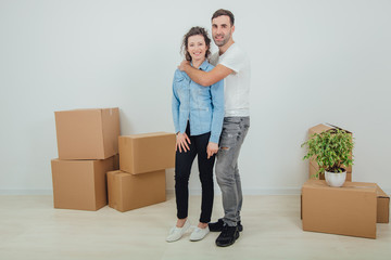 Fototapeta na wymiar Couple moving into their new house, husband is hugging his wife. Room full of boxes.