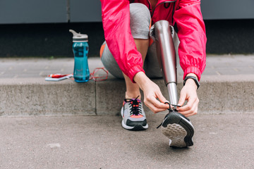 cropped view of disabled sportswoman tying shoelace on street