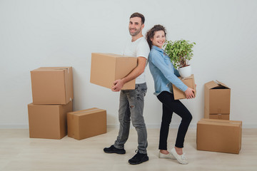 Happy wife and husband holding carton boxes, standing back to back, smiling extremely satisfied to move into new apartment.