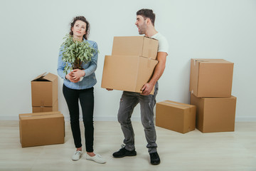 Man can not hold heavy carton boxes anymore, but he doesn't know where to put them. His wife is standing with flowerpot in hands, dreaming.