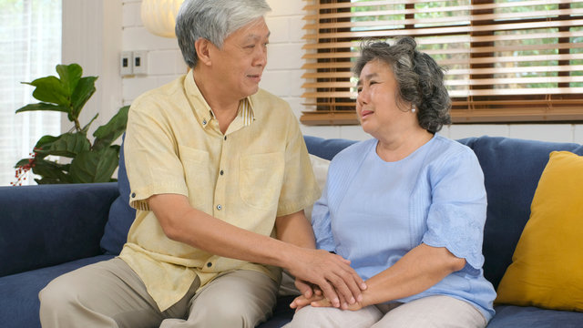 Senior Asian Couple Comforting Each Other From Depressed Emotion While Sitting On Sofa At Home Living Room, Old Retirement Lifestyle