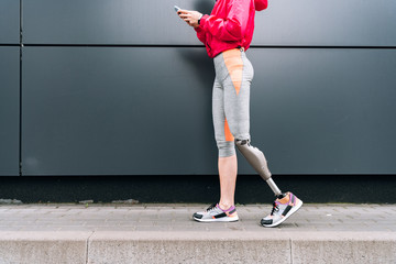 partial view of disabled sportswoman with prosthesis holding smartphone on street