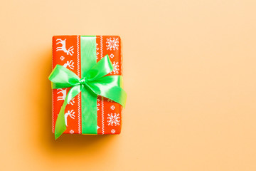 wrapped Christmas or other holiday handmade present in paper with green ribbon on orange...