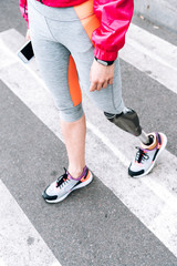 partial view of disabled sportswoman with prosthesis holding smartphone on street