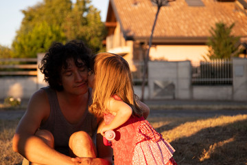 Little toddler daughter kissing her young father at sunset