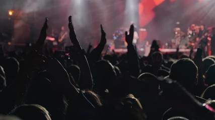 People clap their hands at night rock concert. Group of fans with phones. 4k, UHD