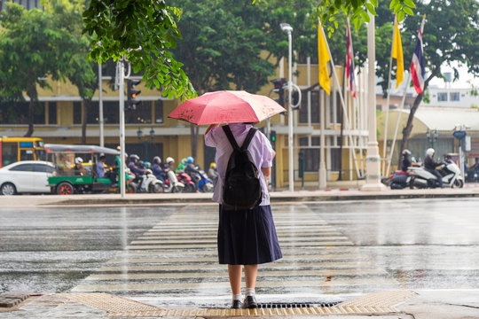 An Asian student girl in unifrom under umbrella waiting for cross road.