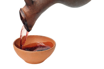 A red wine is pouring from  jug in to the clay cup