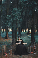 Mysterious model girl with makeup and costume for Halloween. Stylish model girl in the image of Maleficent posing among mystic forest - fairytale story, cosplay.