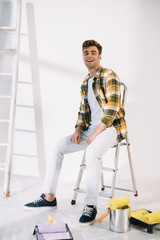 handsome young man smiling while sitting on ladder and looking at camera