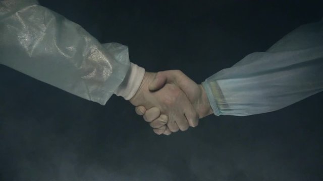 Doctors surgeons shake hands after successful outcome of the operation. Medicine. Black background with smoke. Save a life or kill concept. Surgery and operating table. Slow motion