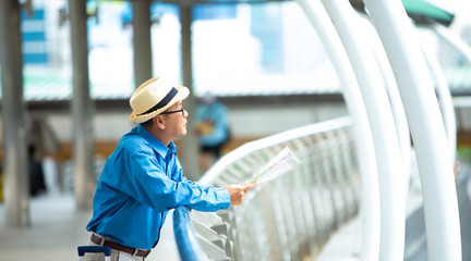 Old senior man of backpackers holding in hands travel map and walking by the city. Happy Travel and tourism concept.