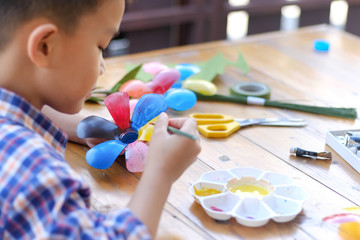 Asian boy painting a colourful plastic flower made from water bottle on wooden table...