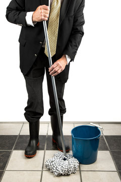 Unidentified Executive Man In A Dark Business Suit And Tie Wearing Black Rubber Boots Mopping  A Tile Floor With A White String Mop And A Blue Bucket