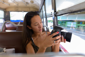 Fototapeta na wymiar Young tourist woman sitting at bus while using DSLR camera