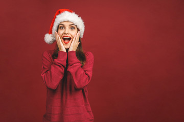 Christmas Santa hat woman portrait. Smiling amazed happy girl isolated against red background. Free copyspace for text. New year concept.