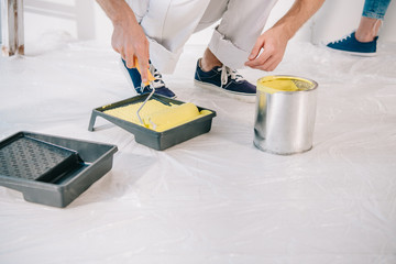 cropped view of man putting paint roller into yellow paint