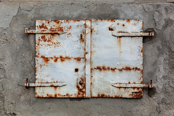 Old, rusty and weathered metal window coverings, closed shut on building exterior