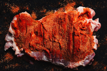 Beautiful piece of raw pork covered in different spices with dominant red color from ground red pepper on a black background