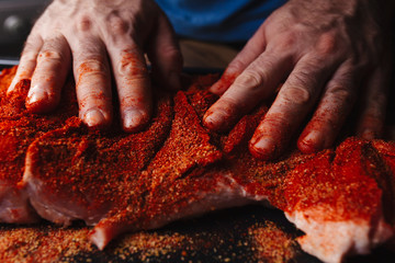 Man preparing raw piece of meat, rubbing different spices and herbs in it before roasting