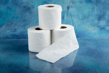 rolls of soft toilet paper on a shiny countertop with a  textured aqua marine blue cloth background