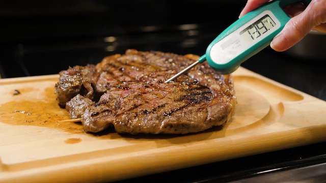 Checking for safe food temperature with digital instant thermometer. Cook measuring temperature of grilled steak on wooden cutting board.