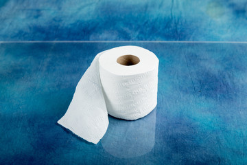 rolls of soft toilet paper on a shiny countertop with a  textured aqua marine blue cloth background