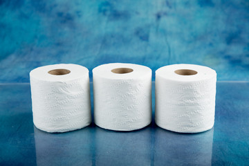 rolls of soft toilet paper on a shiny countertop with a  textured aqua marine blue cloth background
