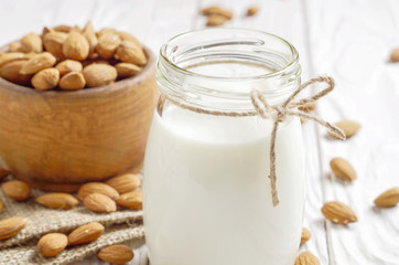 Obraz na płótnie Canvas Milk or yogurt in mason jar on white wooden table with bowl of almonds on hemp napkin aside