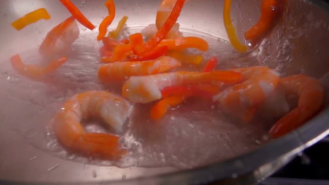 Shrimps and pepper fall into the pan on a heated vegetable oil