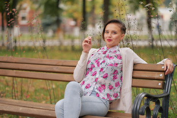 short-haired woman in jeans and a light blouse in the park smokes while sitting on a bench in the autumn park