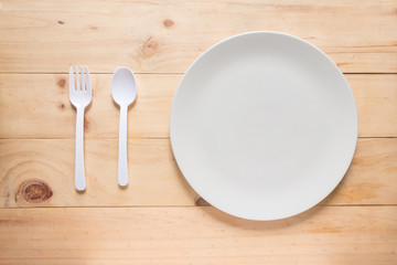 Empty white round dish or plate on wooden background, top view of tableware with copy space, spoon and fork