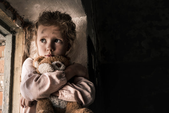 frustrated child holding teddy bear in dirty room, post apocalyptic concept