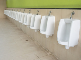 Empty row of outdoor urinals men public toilet and green wall background.Close up white urinals in...