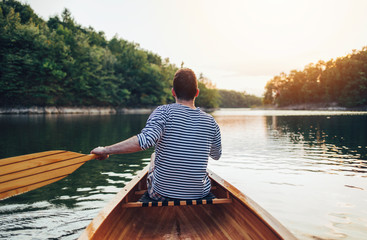 Fototapeta na wymiar Man in sailor shirt paddling canoe on the sunset lake 
