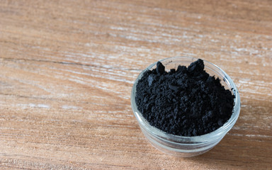Close up of activated black charcoal powder in a glass bowl on wooden background