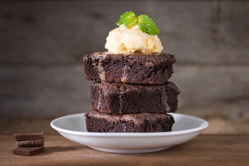 Chocolate brownies stacks and vanila ice cream on top, wooden background