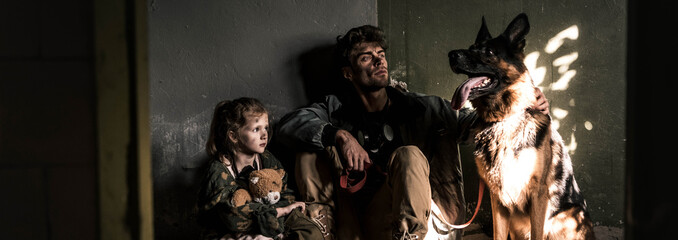 panoramic shot of man and kid sitting with german shepherd dog, post apocalyptic concept