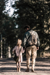 back view of kid holding hands with man while standing on road, post apocalyptic concept