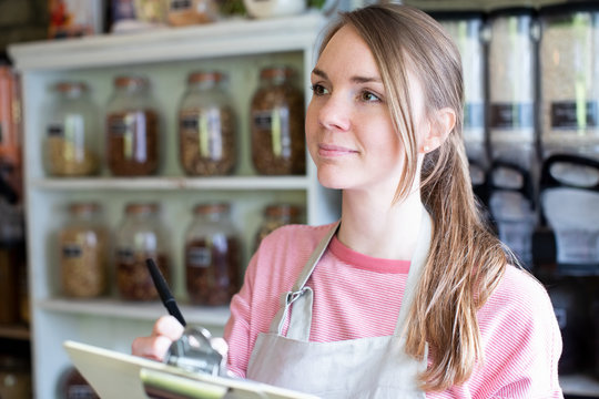 Female Owner Of Sustainable Plastic Free Grocery Store Checking Stock On Shelves