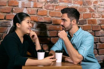 girl talks about something to a a young man sitting at a table in a cafe on the background of a rough brick wall