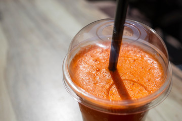 Cold fresh carrot and orange juice in a plastic glass on wooden table
