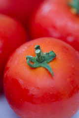 Details of a red tomato with green stipe and other blurry tomatoes in the background